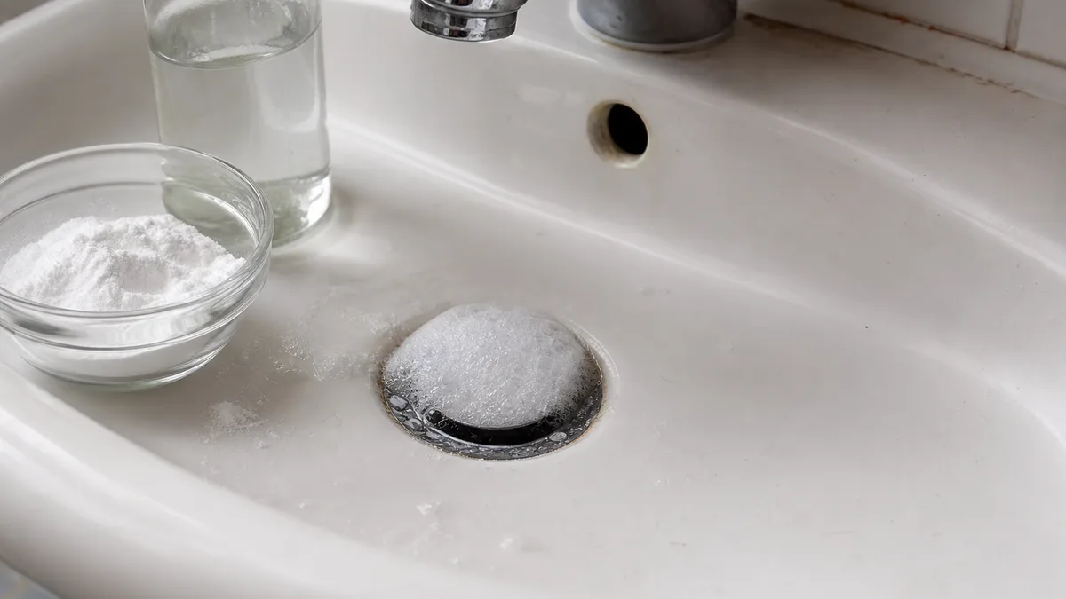 Natron und Essig werden nacheinander in einen Waschbecken-Abfluss gegeben – das entstehende Schaum löst Ablagerungen im Rohr